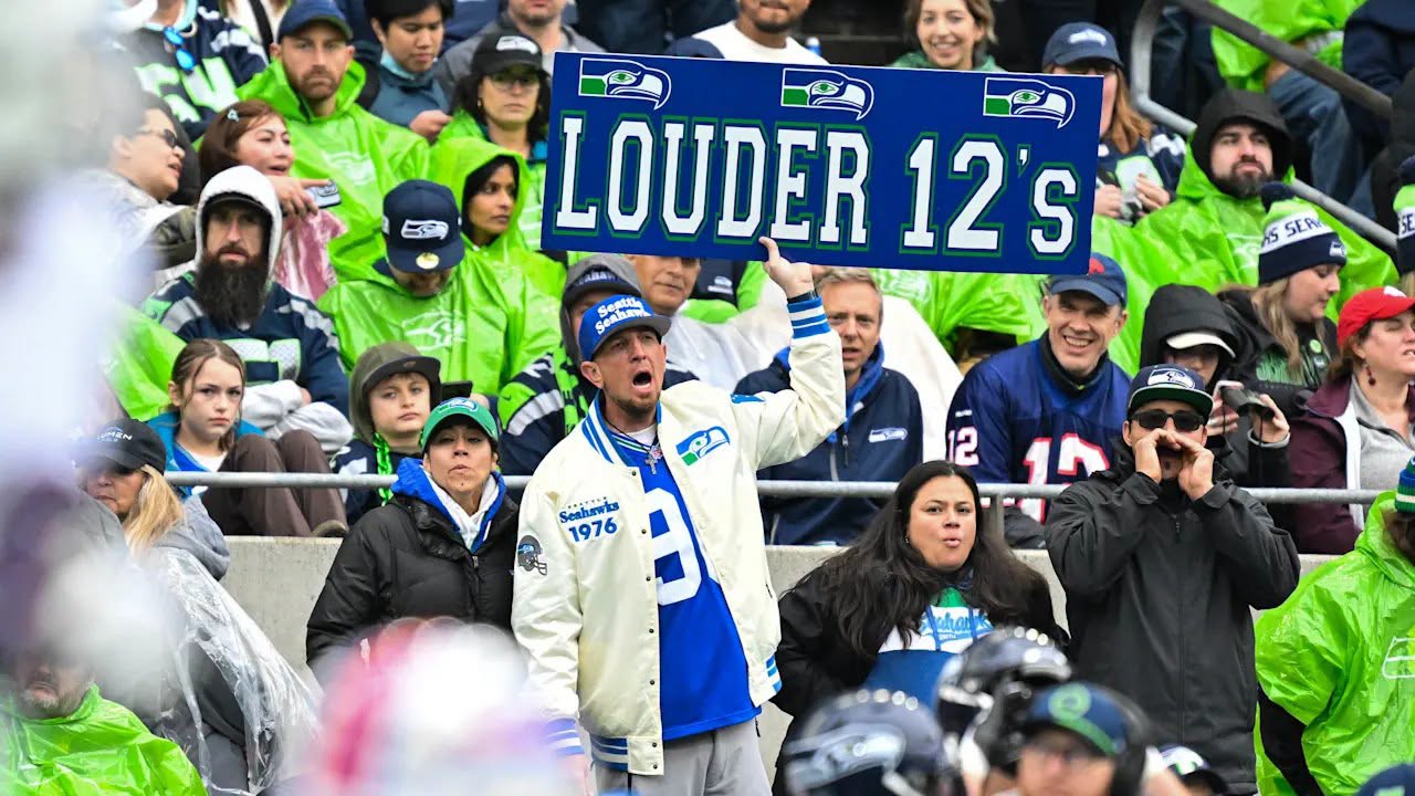 Seahawks fans in the stands holding a Louder 12’s sign